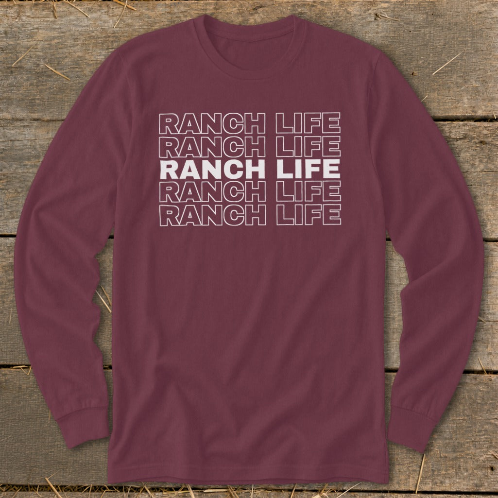 Maroon long-sleeve t-shirt with stacked white outlined text reading RANCH LIFE on a rustic wooden background.