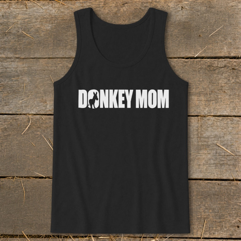 A black tank top with the white text DONKEY MOM, featuring a donkey silhouette inside the letter O, laid on a rustic wooden background.