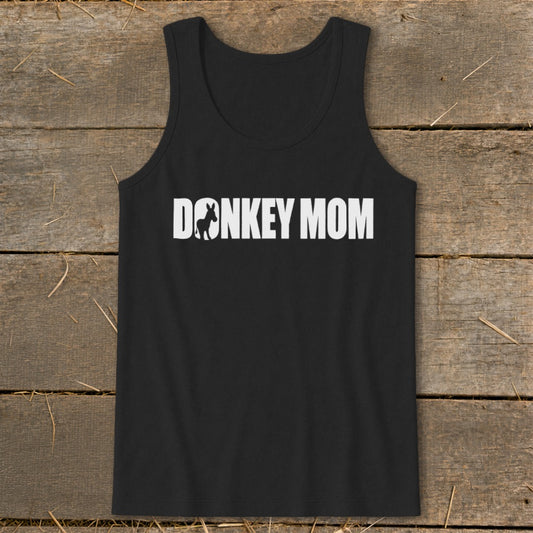 A black tank top with the white text DONKEY MOM, featuring a donkey silhouette inside the letter O, laid on a rustic wooden background.