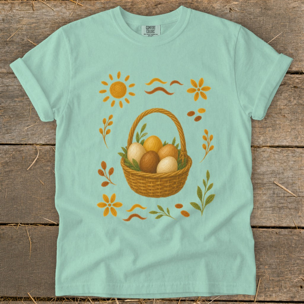 Light blue t-shirt with Easter basket and eggs graphic, sun, flowers, and leaves.