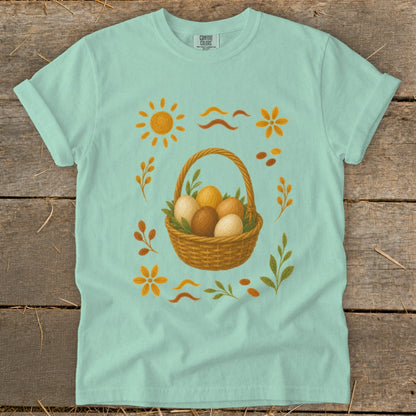 Light blue t-shirt with Easter basket and eggs graphic, sun, flowers, and leaves.