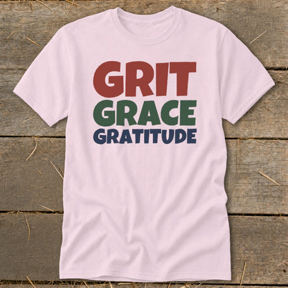 Light pink short-sleeved t-shirt featuring stacked block lettering that reads Grit in red, Grace in green, and Gratitude in blue.