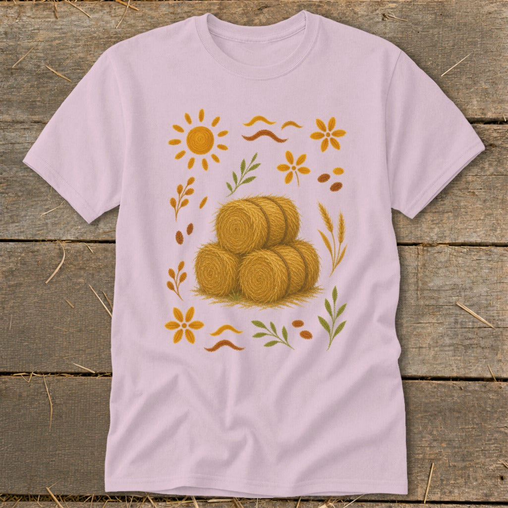 Light pink t-shirt with stacked hay bales, sun, flowers, and leaves graphic.