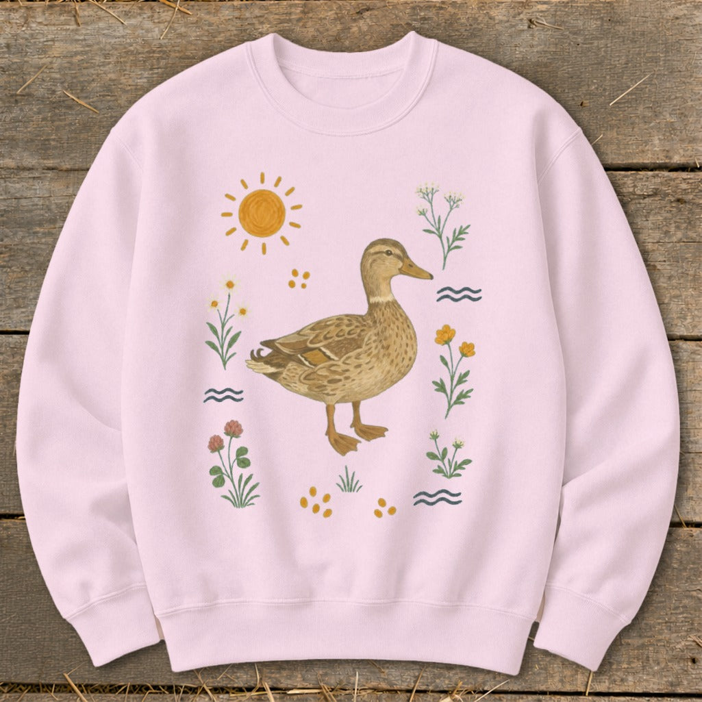 Pink sweatshirt with a watercolor illustration of a mallard duck surrounded by flowers and sun.
