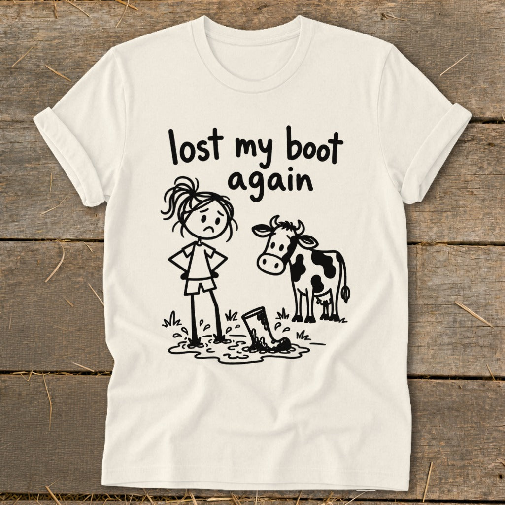Off-white t-shirt featuring a cartoon illustration of a sad girl and a cow looking at a muddy boot, with the text "lost my boot again."