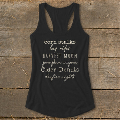 Black tank top with list of fall activities: corn stalks, hay rides, harvest moon, pumpkin wagons, cider donuts, bonfire nights.