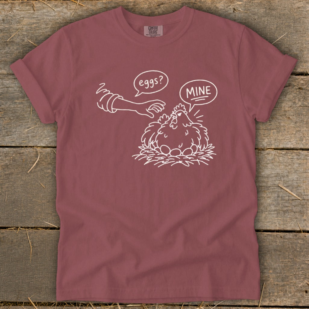 T-shirt with white line drawing of a chicken protecting its eggs, saying "MINE".