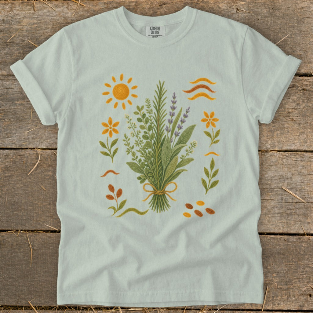 Light blue t-shirt with a botanical illustration of herbs, flowers, and sun.