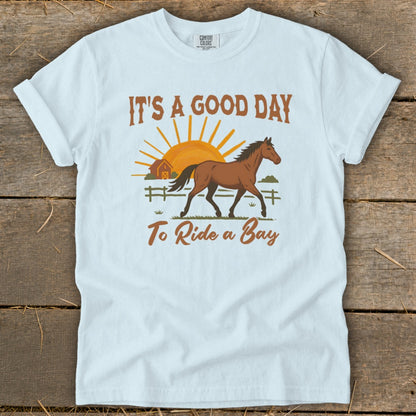 Light blue t-shirt with a bay horse, barn, sun, and text "IT'S A GOOD DAY To Ride a Bay".