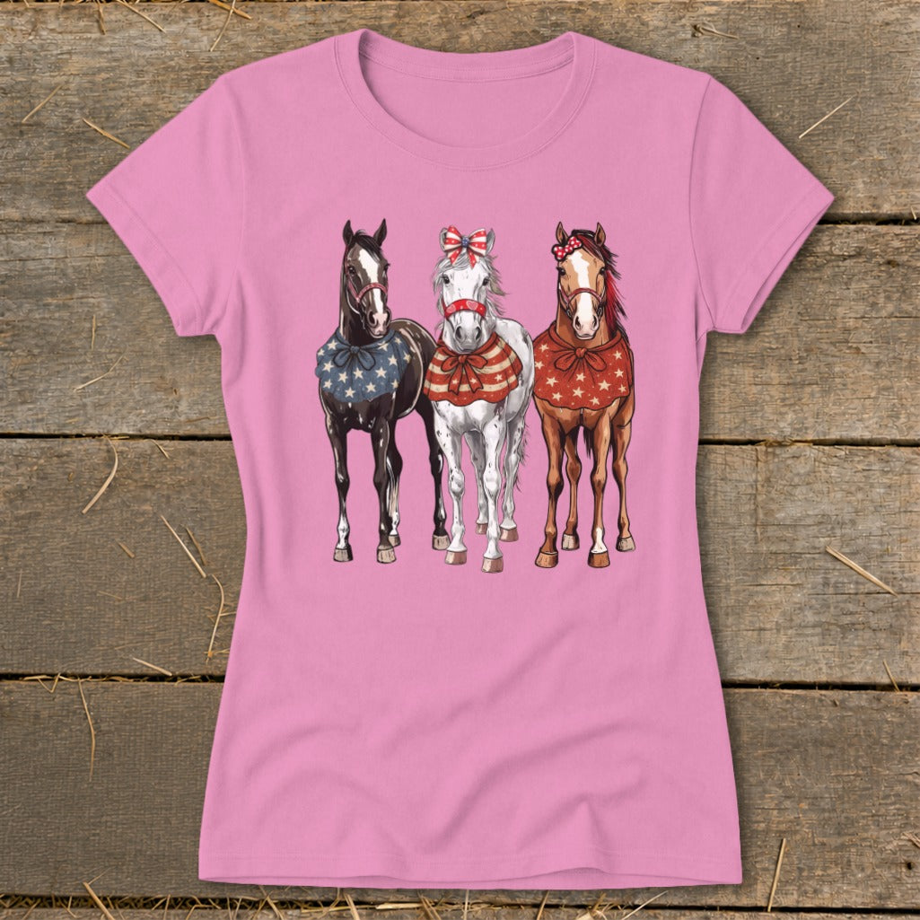 Three horses in patriotic bandanas and bows stand on a pink t-shirt.