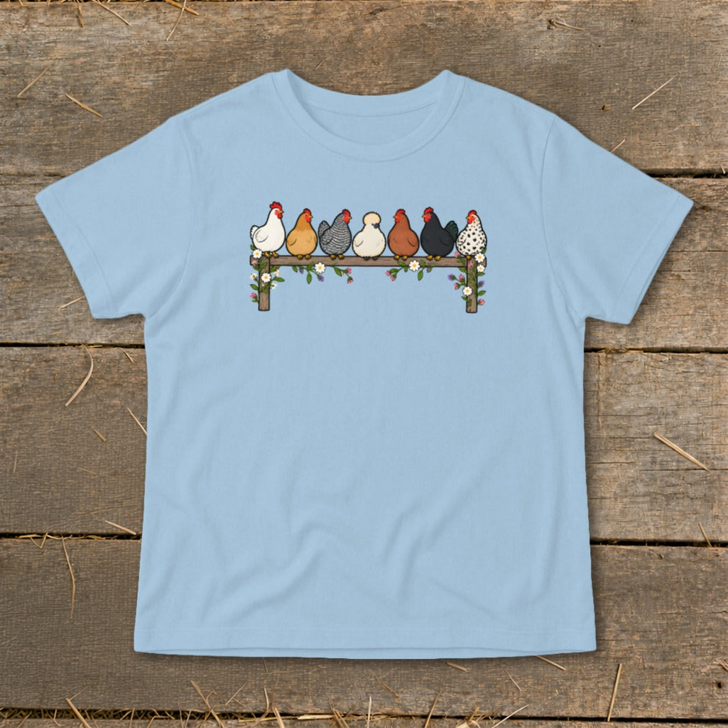 A light blue t-shirt printed with an illustration of seven colorful chickens roosting on a wooden fence.