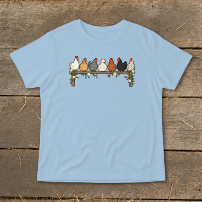 A light blue t-shirt printed with an illustration of seven colorful chickens roosting on a wooden fence.