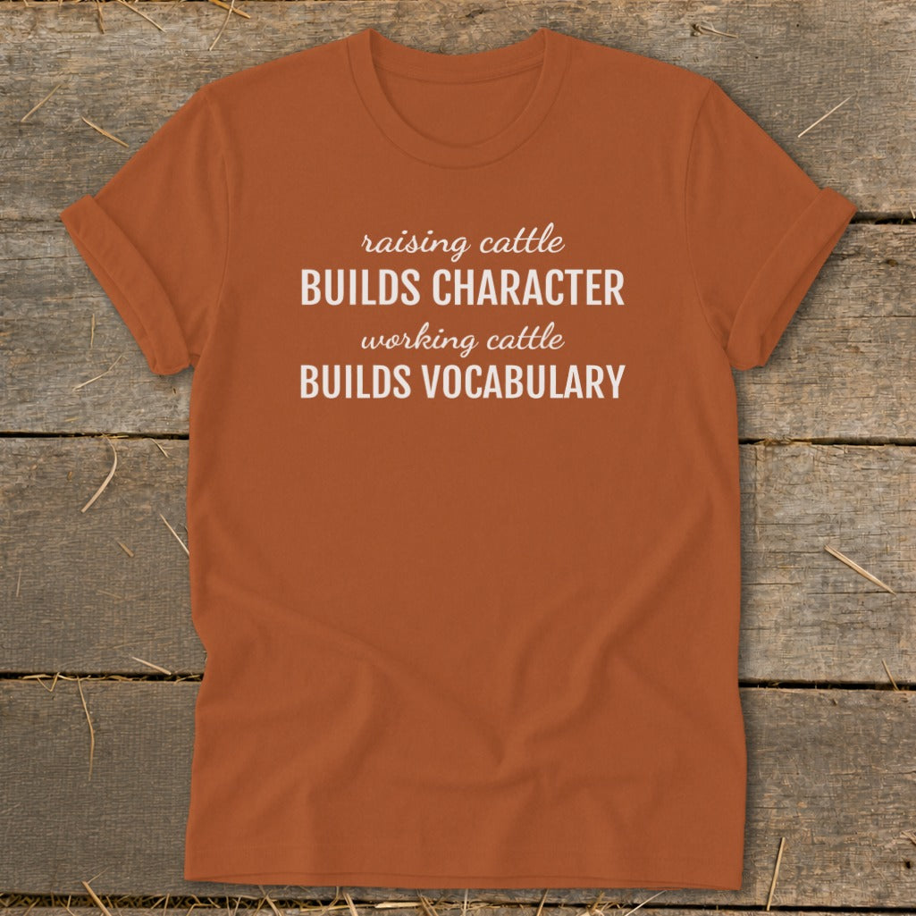 Orange t-shirt with white text: "raising cattle BUILDS CHARACTER working cattle BUILDS VOCABULARY"