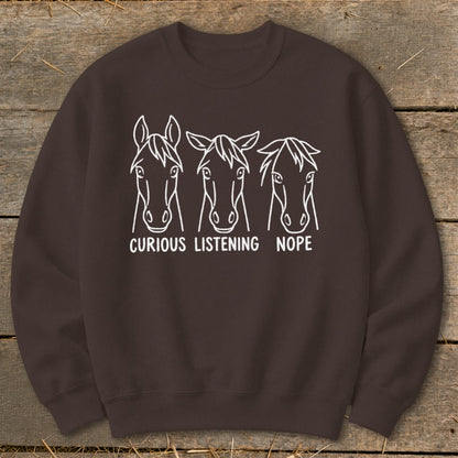 Brown crewneck sweatshirt featuring white line art of three horse heads with text reading curious, listening, and nope.