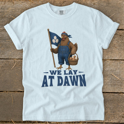 Chicken in overalls holding flag and basket of eggs with text "We Lay At Dawn".