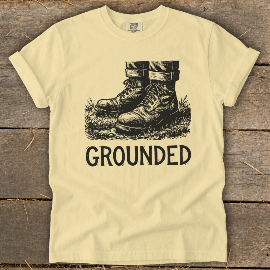 Light yellow t-shirt with black graphic of boots and the word GROUNDED.