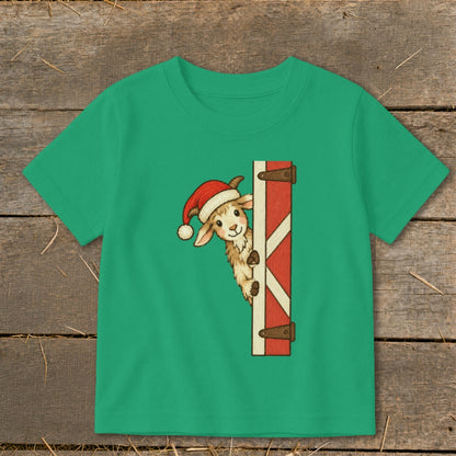 Green t-shirt with a cartoon goat wearing a Santa hat peeking from behind a barn door.