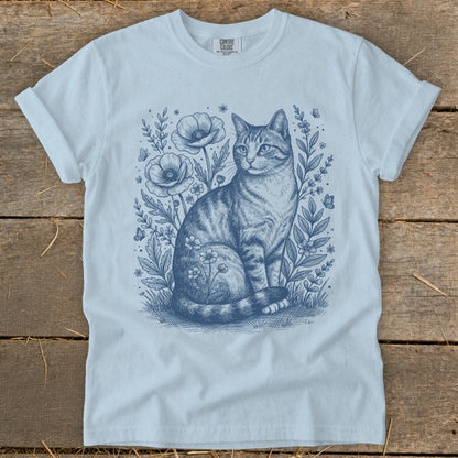 T-shirt with blue line drawing of a tabby cat sitting among flowers and butterflies.