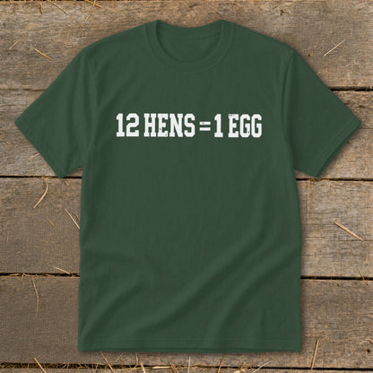 Dark green short-sleeve t-shirt with white block lettering that reads 12 HENS = 1 EGG laid flat on a rustic wooden background.