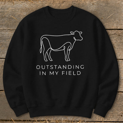 Black sweatshirt with white line drawing of a cow and text "OUTSTANDING IN MY FIELD".