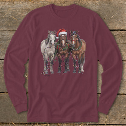 Three horses, one wearing a Santa hat, are decorated with Christmas lights and wreaths.