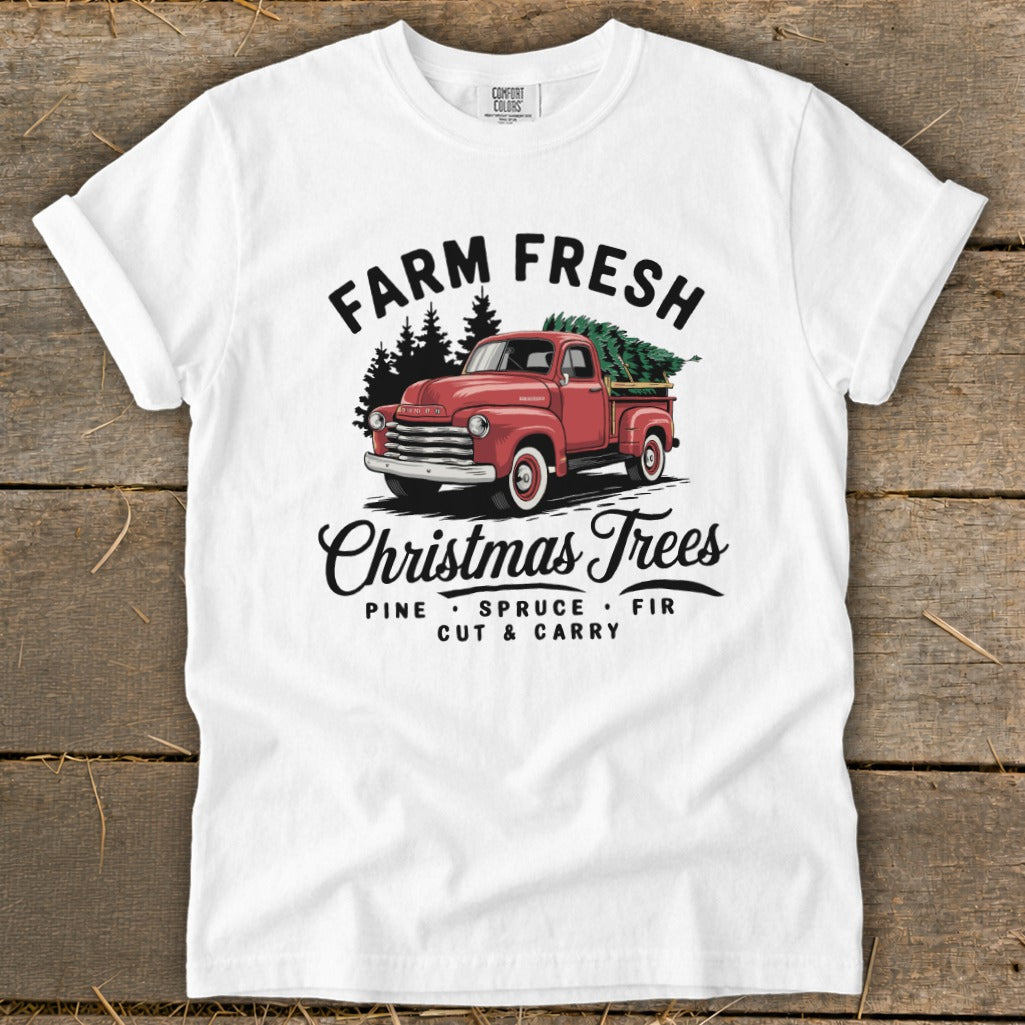 White t-shirt with vintage red truck, pine trees, and "Farm Fresh Christmas Trees" text.