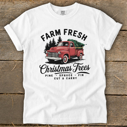 White t-shirt with vintage red truck, pine trees, and "Farm Fresh Christmas Trees" text.