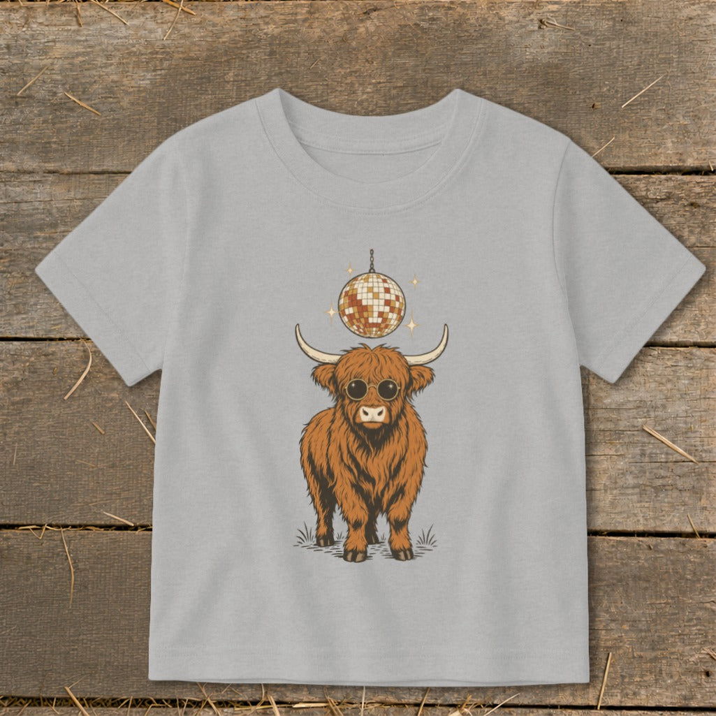 Highland cow wearing sunglasses under a disco ball on a light gray t-shirt.