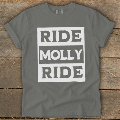 A gray t-shirt with a white block graphic reading RIDE MOLLY RIDE laid flat on wood.