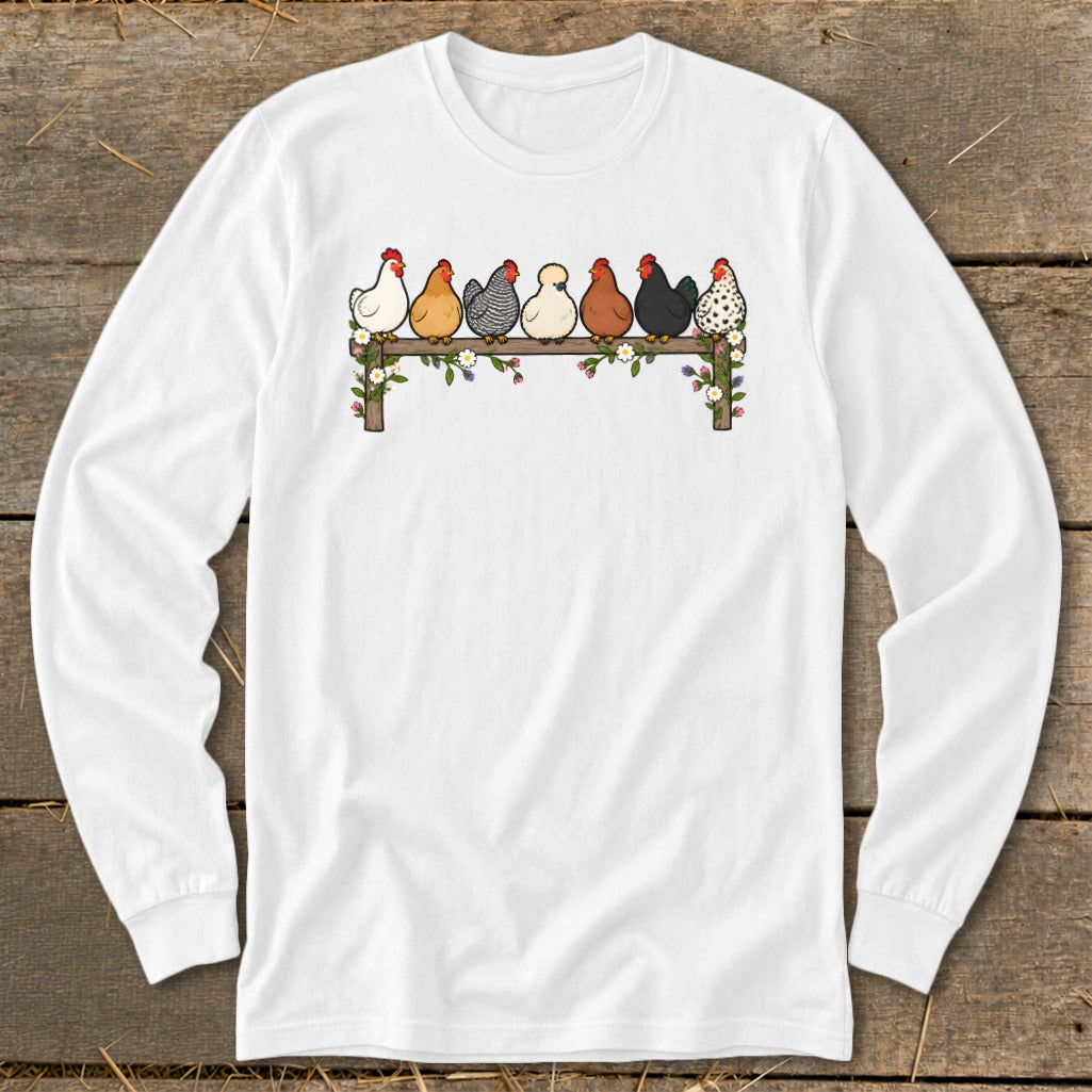 A white long-sleeve t-shirt with a cartoon graphic of seven colorful chickens sitting on a wooden fence.