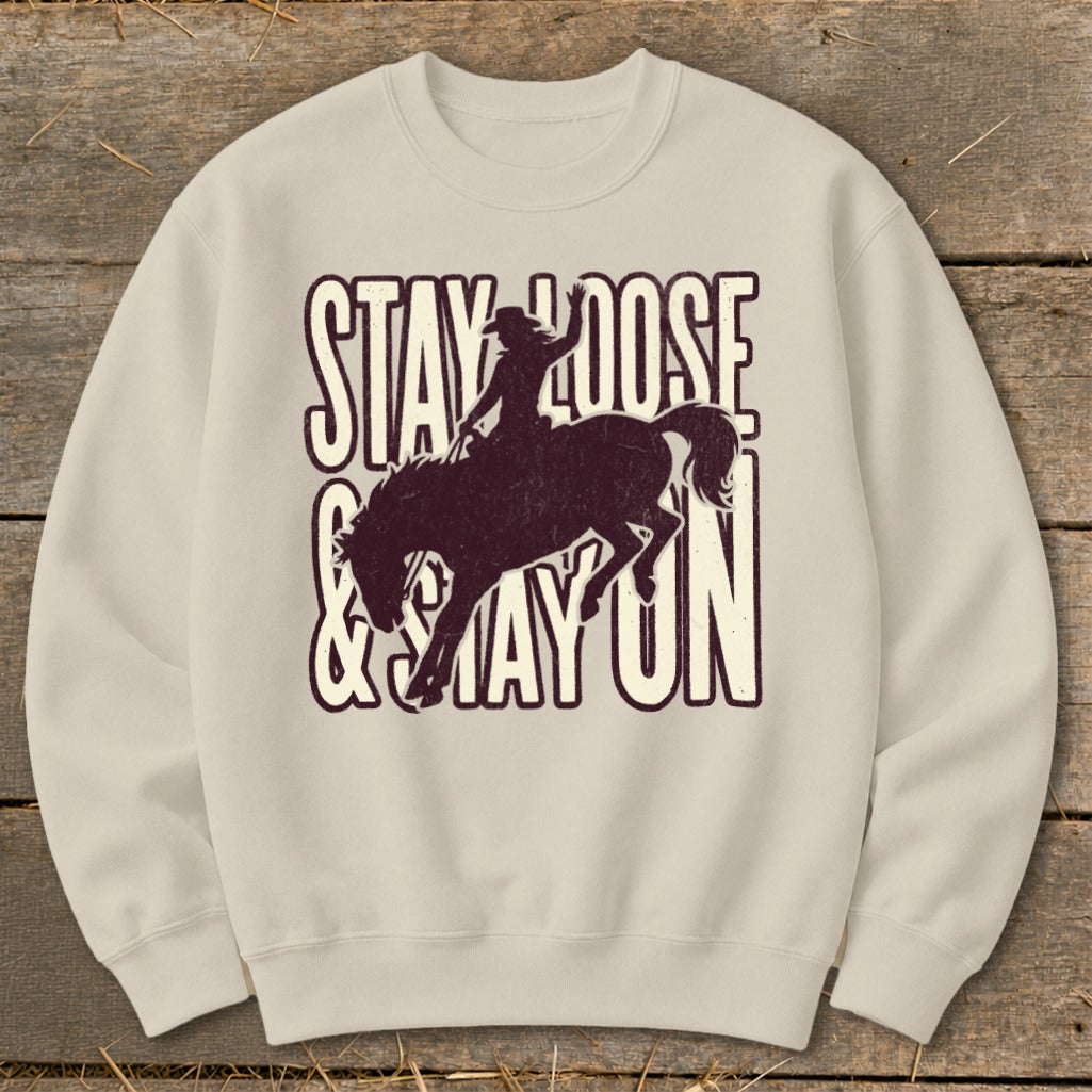 Light beige sweatshirt with distressed graphic of a bucking bronco and rider, text "STAY LOOSE & STAY ON".