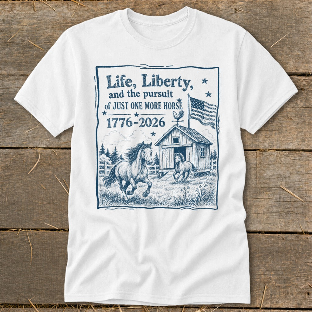 White t-shirt with illustration of horses, barn, US flag, and text "Life, Liberty, and the pursuit of JUST ONE MORE HORSE 1776-2026".