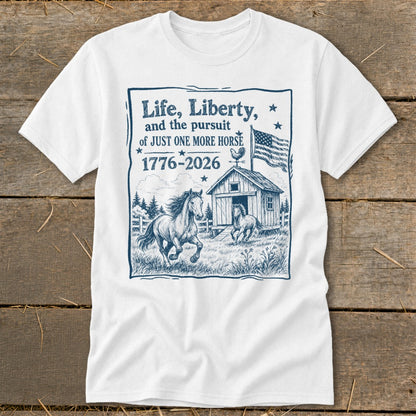 White t-shirt with illustration of horses, barn, US flag, and text "Life, Liberty, and the pursuit of JUST ONE MORE HORSE 1776-2026".