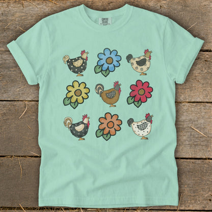 Mint t-shirt with nine folk art chickens and flowers in a grid pattern.