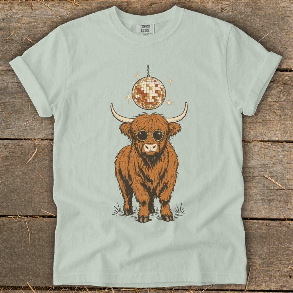 Highland cow with sunglasses and disco ball graphic on a light green t-shirt.
