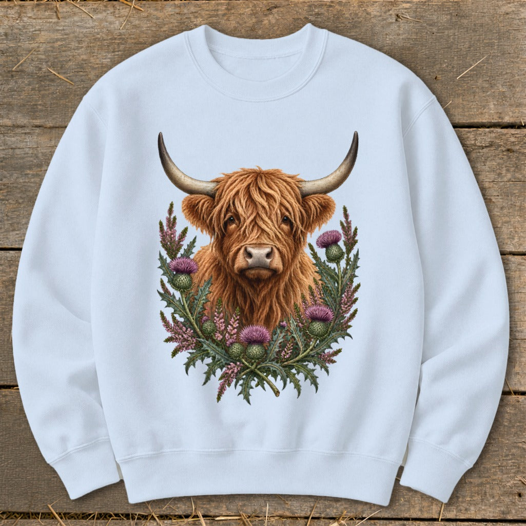 Highland cow with horns surrounded by thistles on a light blue sweatshirt.