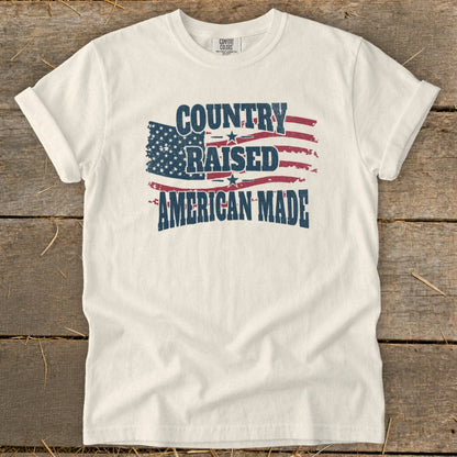 White t-shirt with "Country Raised American Made" text and distressed American flag design.