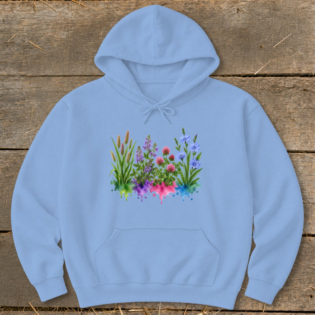 A light blue hooded sweatshirt featuring a colorful watercolor botanical graphic on a rustic wooden background.