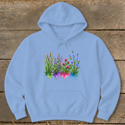 A light blue hooded sweatshirt featuring a colorful watercolor botanical graphic on a rustic wooden background.