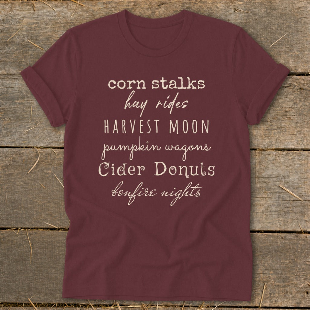 Maroon t-shirt with "corn stalks, hay rides, Harvest Moon, pumpkin wagons, Cider Donuts, bonfire nights" text.