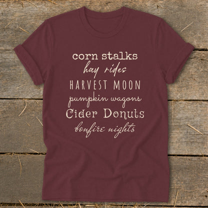Maroon t-shirt with "corn stalks, hay rides, Harvest Moon, pumpkin wagons, Cider Donuts, bonfire nights" text.