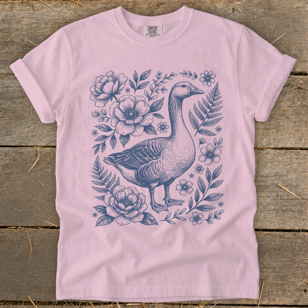 Pink t-shirt with a detailed blue ink illustration of a goose surrounded by flowers and ferns.