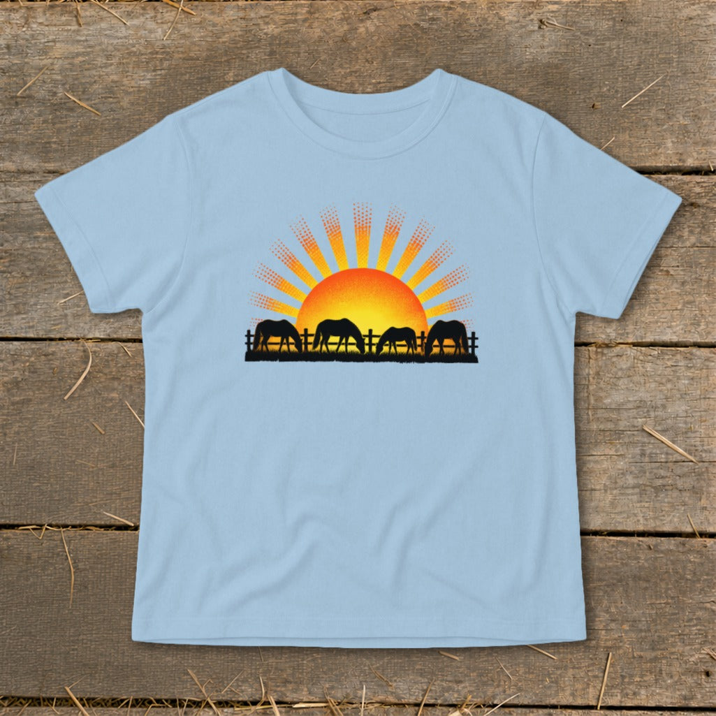 Silhouette of horses grazing in front of a rising sun with radiating rays.