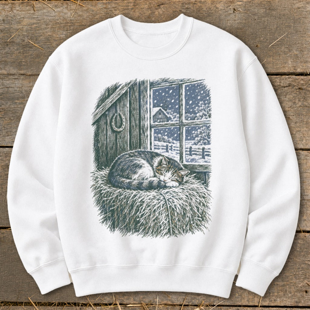 White sweatshirt with a print of a sleeping cat on hay in front of a snowy window.