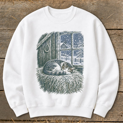 White sweatshirt with a print of a sleeping cat on hay in front of a snowy window.