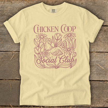 Light yellow t-shirt with purple "CHICKEN COOP Social Club" graphic featuring a chicken and flowers.