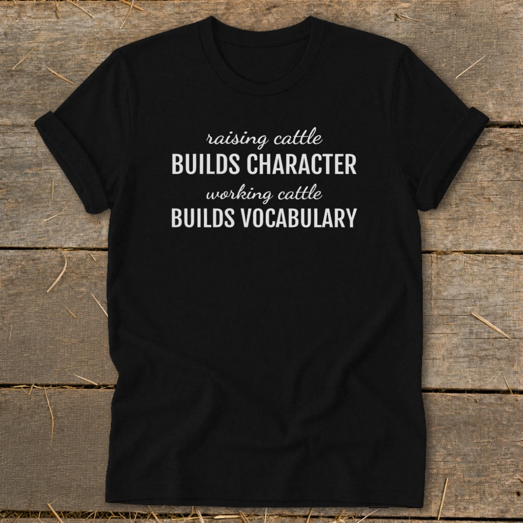 Black t-shirt with white text: "raising cattle BUILDS CHARACTER, working cattle BUILDS VOCABULARY".