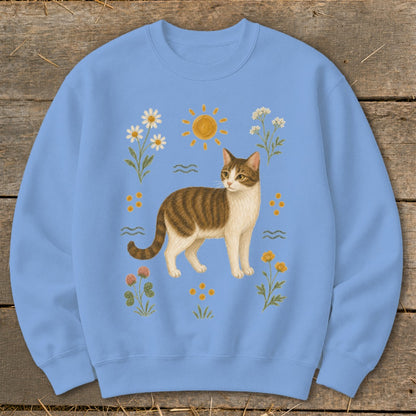 Tabby cat illustration with sun and wildflowers on a light blue sweatshirt.