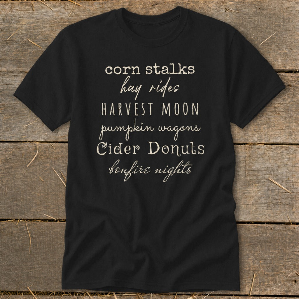 Black t-shirt with list of autumn phrases: corn stalks, hay rides, harvest moon, pumpkin wagons, cider donuts, bonfire nights.