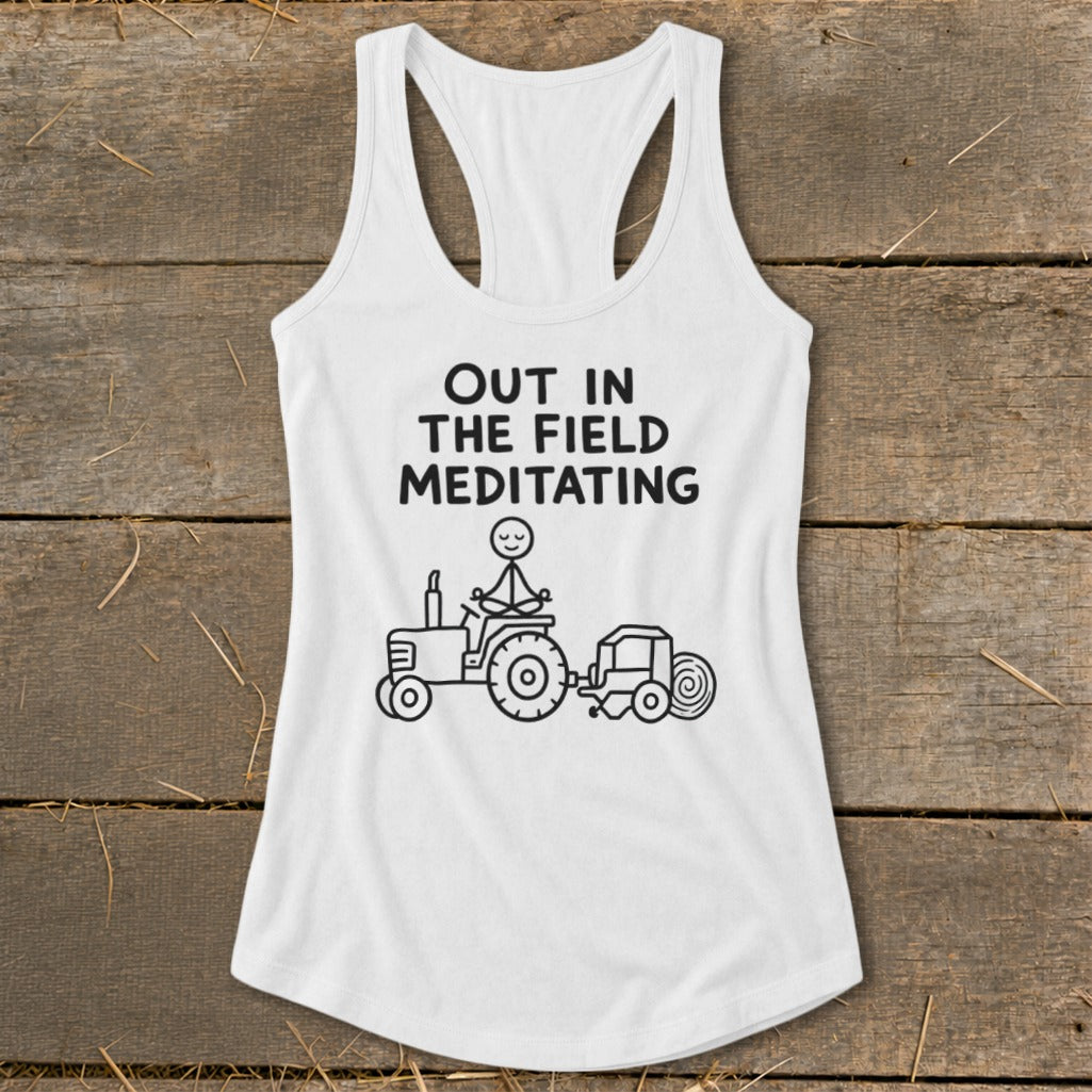 White tank top with "Out In The Field Meditating" text and stick figure on tractor.